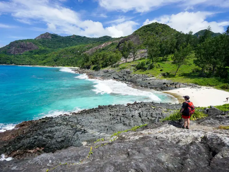 Wanderer mit Blick auf eine abgelegene Bucht mit weißem Sandstrand und türkisfarbenem Wasser.