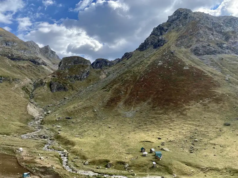 Gebirgstal mit Hütten und Bachlauf.