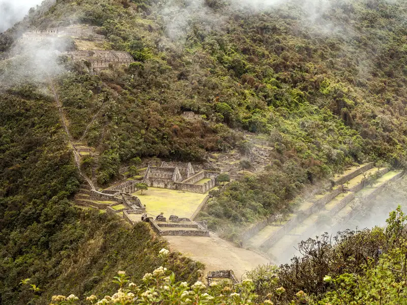 Alte Inka-Terrassen und -Strukturen, umgeben von üppiger Vegetation und teilweise verdeckt durch Nebel.