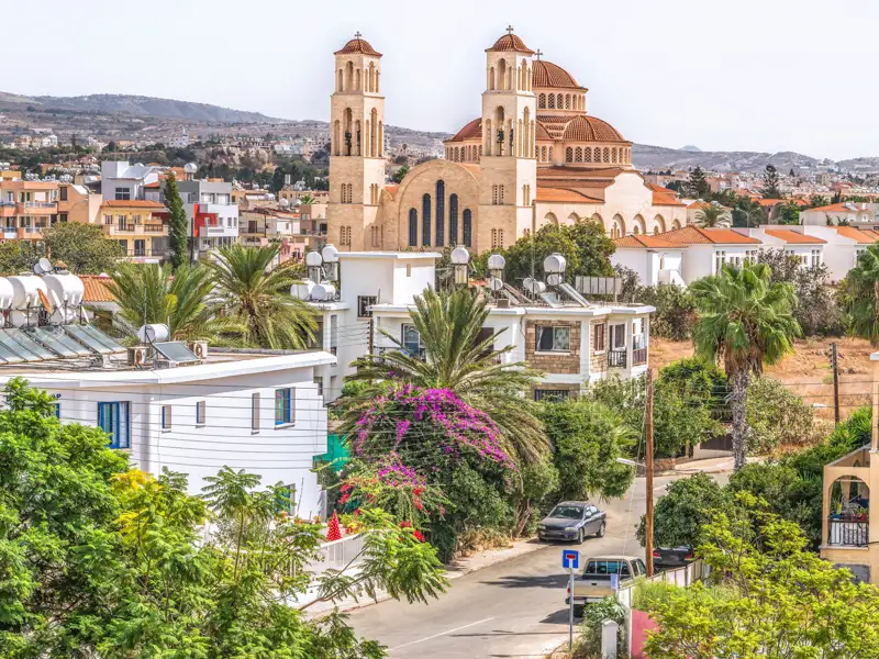Eine Kirche in einer Stadt auf Zypern, umgeben von Wohngebäuden und Palmen.