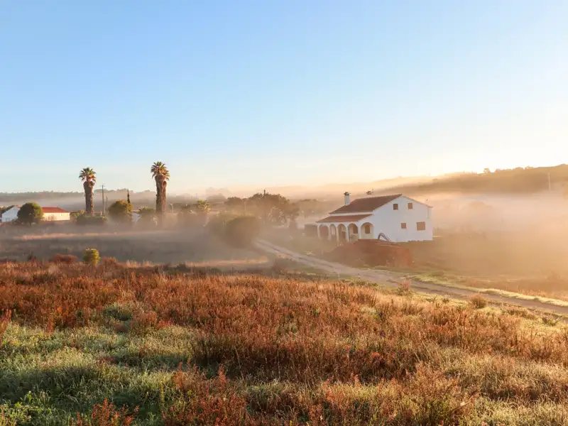 Sonnenaufgang über einem Haus in ländlicher Umgebung.