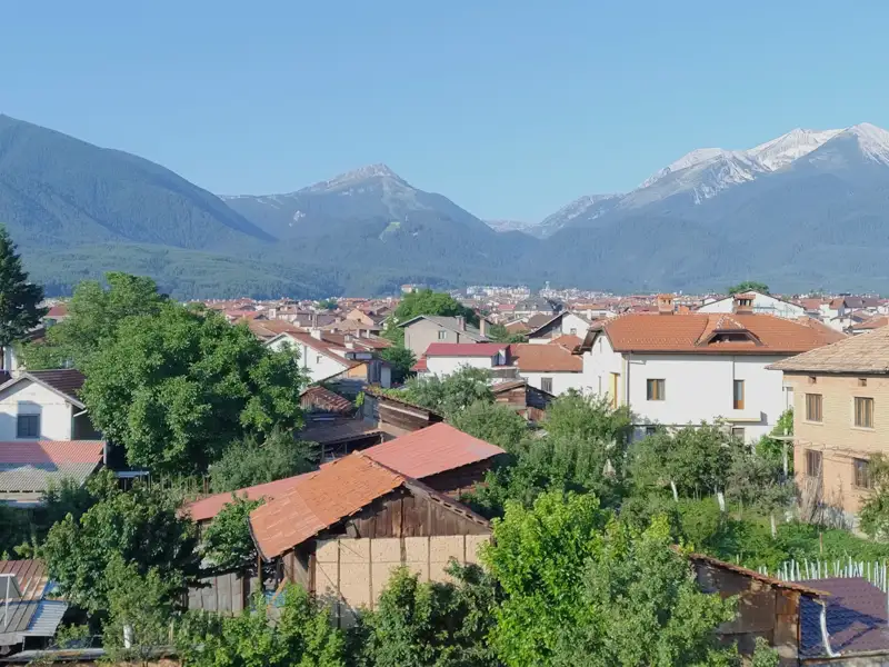 Panoramablick auf eine Stadt in einem Tal, umgeben von bewaldeten Hügeln und schneebedeckten Bergen.