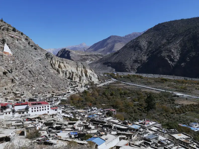 Blick auf ein Bergdorf mit traditionellen Häusern und einem Fluss im Tal.