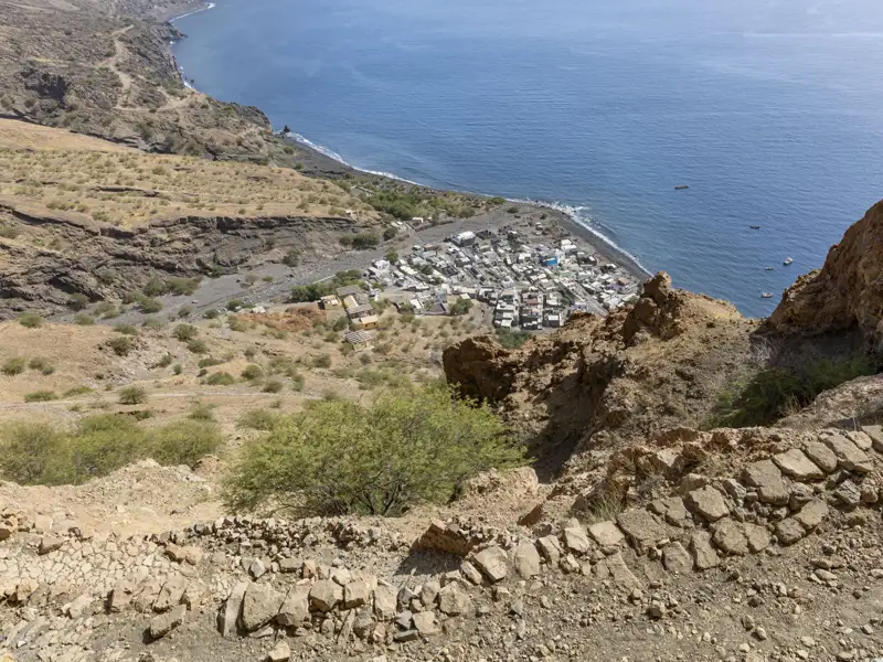 Blick von einem steilen Pfad auf eine Küstensiedlung und das Meer.