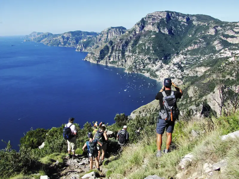 Wanderer mit Rucksäcken auf einem Bergpfad mit Blick auf die Küste und das tiefblaue Meer.