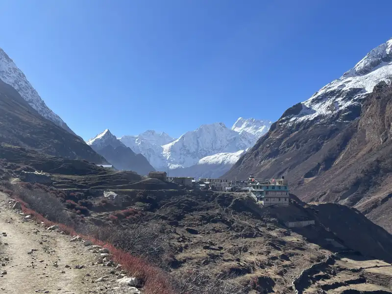 Bergdorf im Himalaya mit schneebedeckten Gipfeln im Hintergrund.