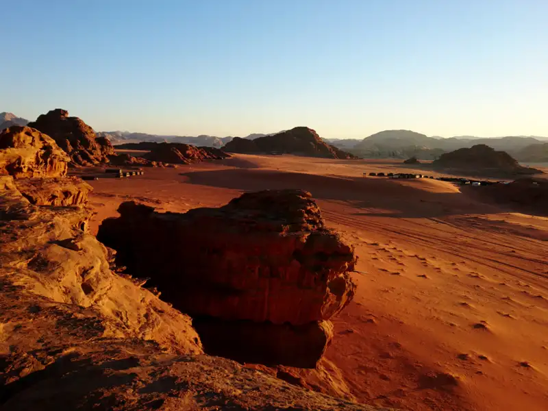 Panorama der Wüste mit Sanddünen, Felsformationen und einem Camp im Hintergrund.