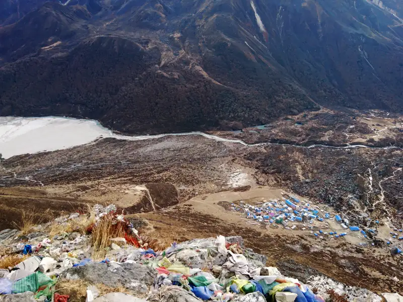Gebetsfahnen markieren einen Aussichtspunkt mit Blick auf ein Hochtal, einen Fluss und eine Siedlung.
