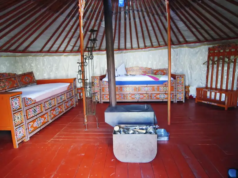 Traditionelle Jurtenunterkunft mit Betten und Ofen.