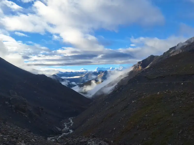 Gebirgstal mit Fluss und schneebedeckten Gipfeln im Hintergrund.