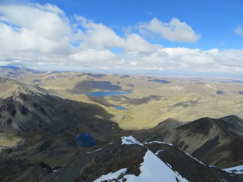 Aussicht von einem Berggipfel auf eine Hochgebirgslandschaft mit Seen und Tälern.