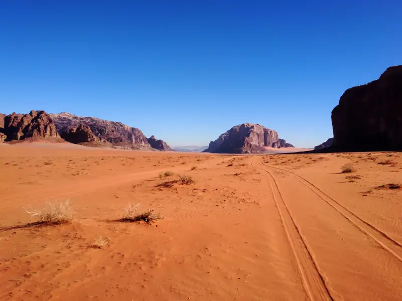 Offroad-Spuren durch die roten Sanddünen einer Wüste, umgeben von markanten Felsformationen.