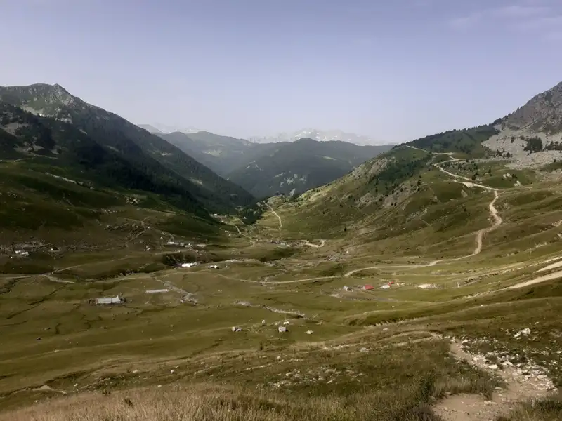 Blick auf ein Bergtal mit grünen Hängen und einem gewundenen Pfad.