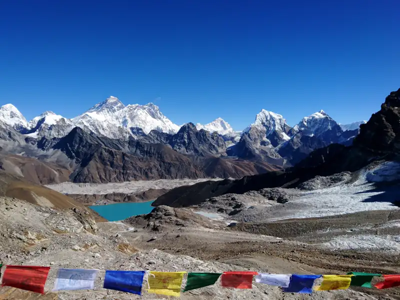 Gebetsfahnen im Vordergrund einer Himalaya-Berglandschaft mit Gletscher und See.