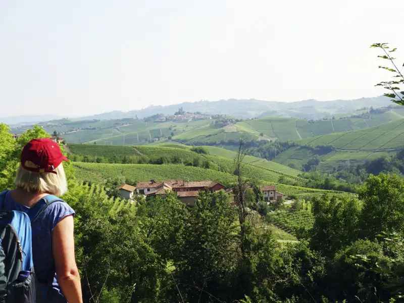 Wanderer betrachtet die Weinberge und ein Dorf in der Hügellandschaft.
