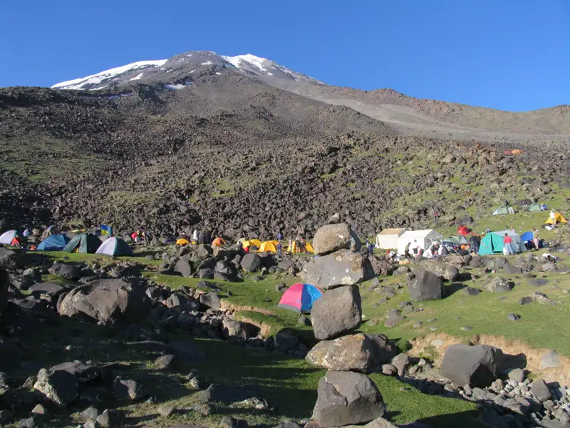 Basislager mit Zelten und Bergsteigern, bereit für die Besteigung des schneebedeckten Berges.