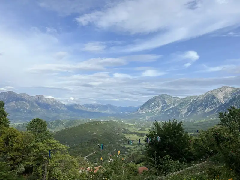 Aussicht auf ein Gebirgstal mit bewaldeten Hängen und Bergen im Hintergrund.