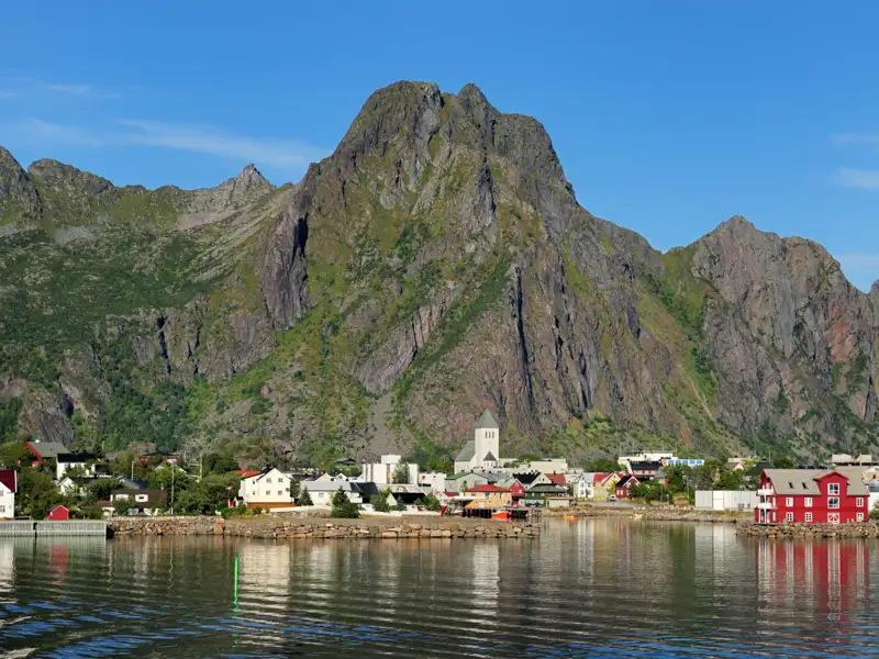 Ansicht einer Küstenstadt mit Häusern, einer Kirche und imposanten Bergen im Hintergrund.