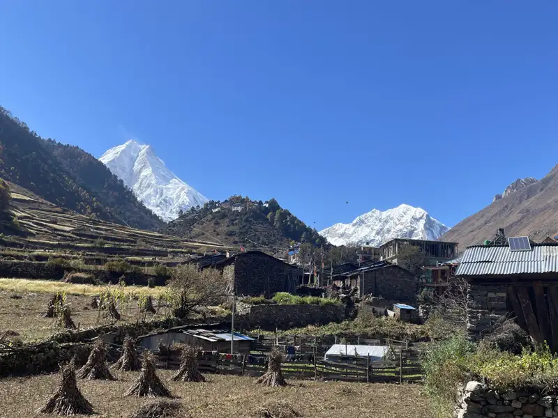 Bergdorf mit schneebedeckten Gipfeln im Hintergrund.