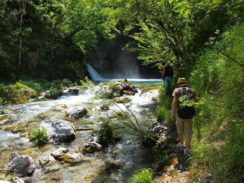 Wanderer auf einem Flussweg in der Nähe eines Wasserfalls.