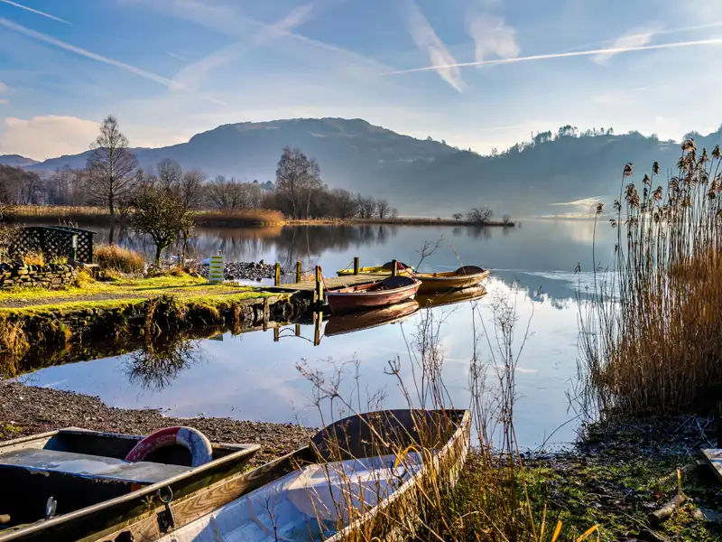 Ruhige Szene am See mit Booten am Ufer und Hügeln im Hintergrund.