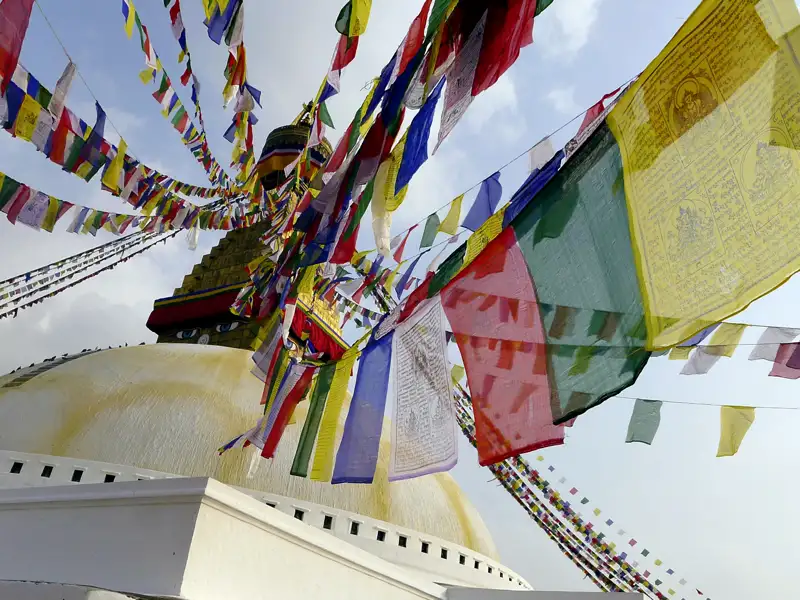 Nahaufnahme von Gebetsfahnen, die über einer Stupa hängen.