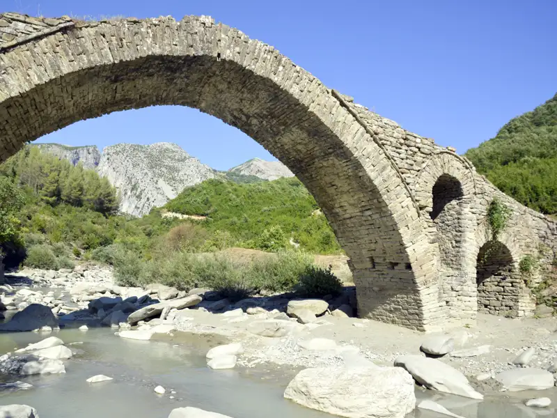 Alte Steinbrücke über einen Fluss in bergiger Landschaft.