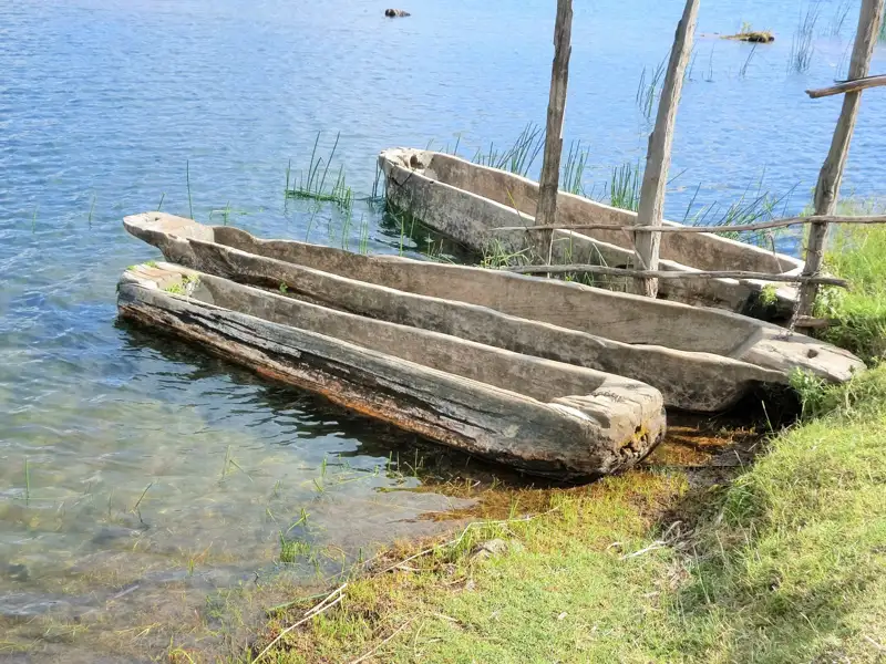 Drei hölzerne Einbäume am Seeufer.