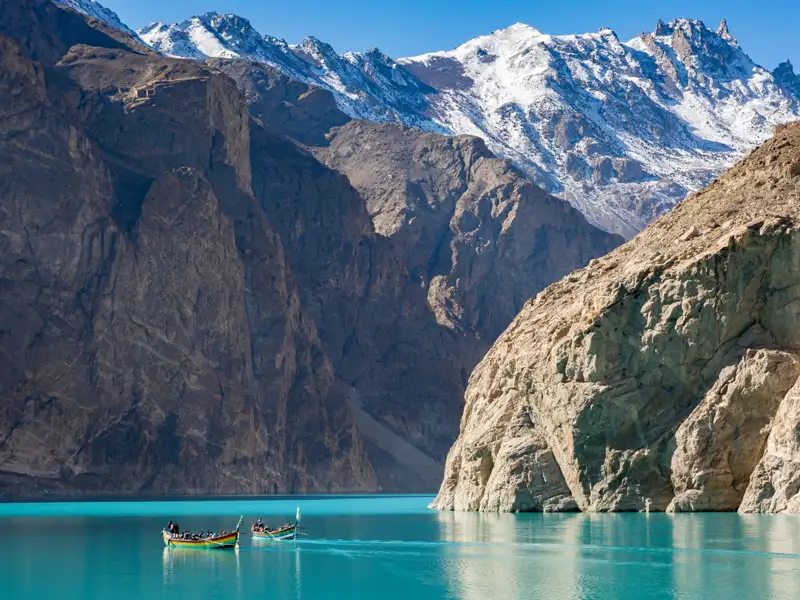 Boote auf einem türkisfarbenen See inmitten einer Berglandschaft.