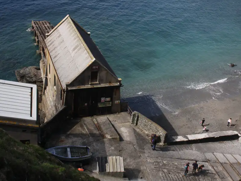 Historisches Bootshaus von 1914 an der Küste mit Besuchern am Strand.