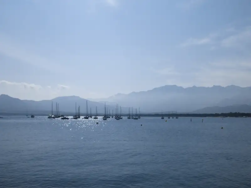 Ruhige Bucht mit Segelbooten und Bergen im Hintergrund.