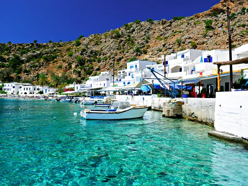 Weiß getünchte Häuser säumen die Küste eines idyllischen Hafens mit türkisfarbenem Wasser.