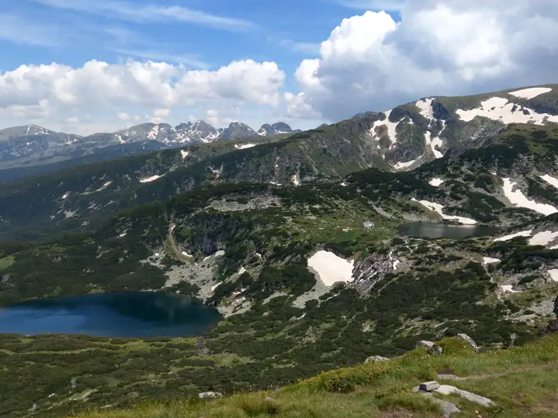 Zwei Bergseen inmitten einer grünen Landschaft mit schneebedeckten Gipfeln im Hintergrund.