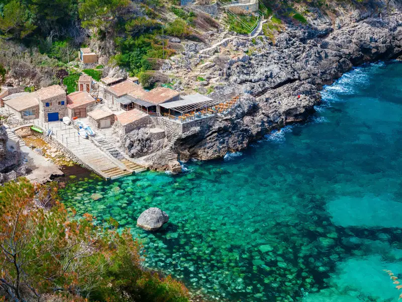 Kleine Bucht mit Gebäuden und kristallklarem, türkisfarbenem Wasser.