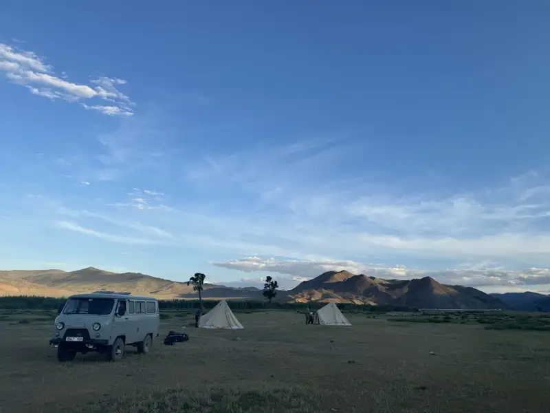 Campingplatz mit Van und Zelten in einer bergigen Landschaft.