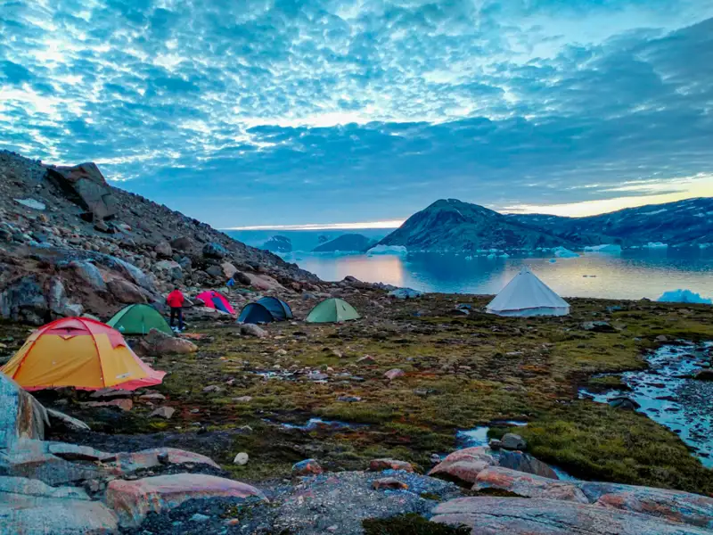 Campingplatz mit Zelten in Grönland, Eisberge im Hintergrund.