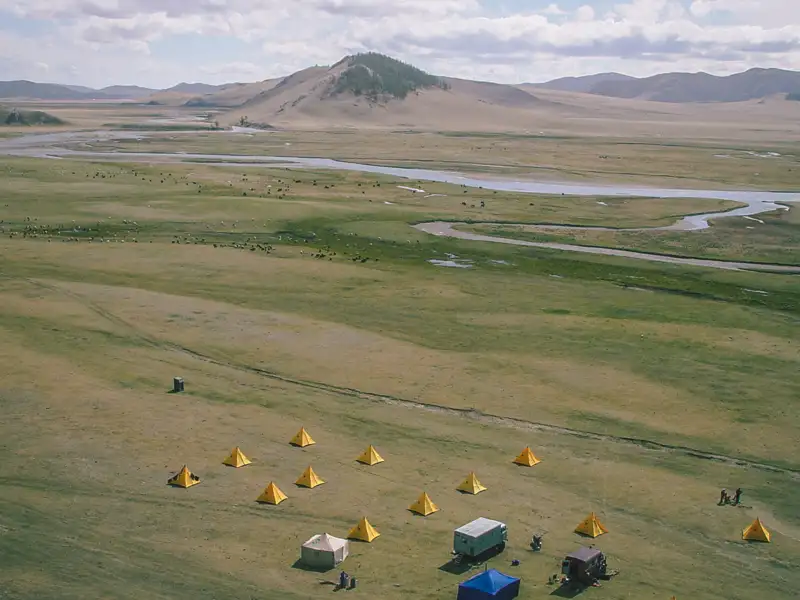 Blick auf das Reisecamp mit Zelten in der Nähe eines Flusses und Hügellandschaft.