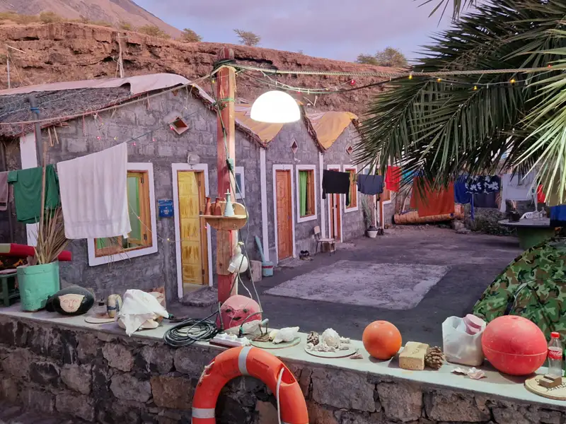 Einfache Unterkünfte am Fuße eines Berges mit Wäscheleinen und maritimen Dekorationen.