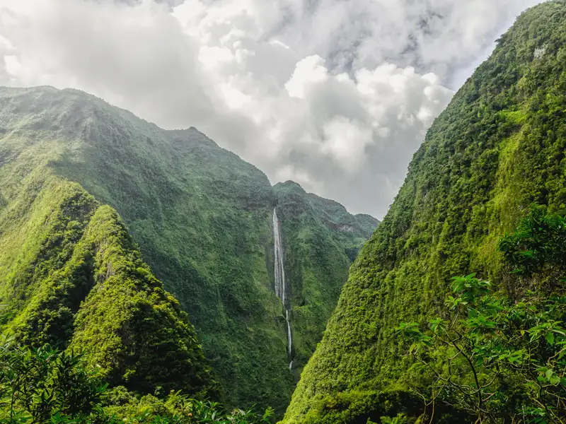 Spektakulärer Wasserfall, der zwischen zwei üppig bewachsenen Bergen inmitten einer dramatischen Landschaft hinabstürzt.