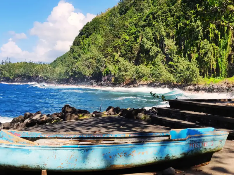 Blaues Fischerboot an einem tropischen Strand mit bewaldeten Hügeln im Hintergrund.