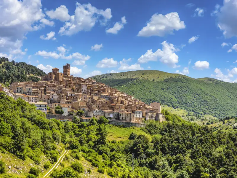 Panoramablick auf ein italienisches Bergdorf mit umliegenden Hügeln und bewaldetem Gelände.