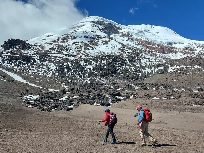 Zwei Wanderer auf einer Bergwanderung nähern sich einem schneebedeckten Gipfel.