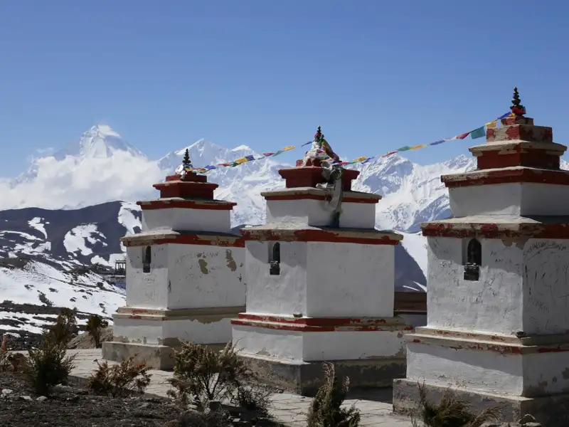 Drei Chortens mit Gebetsfahnen vor einer Bergkette im Himalaya.