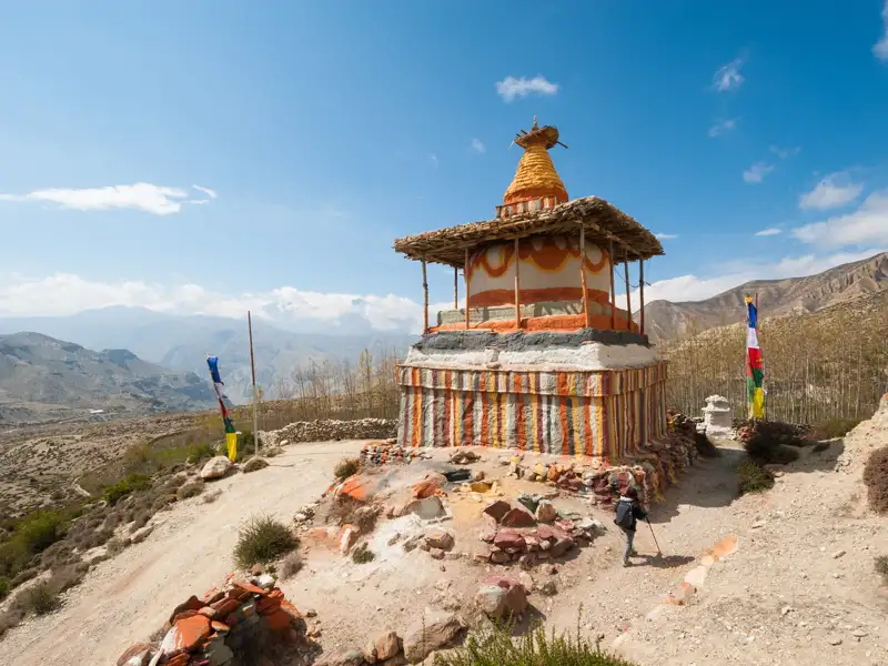 Traditioneller Stupa mit bunten Streifen und Gebetsfahnen in einer Bergregion.
