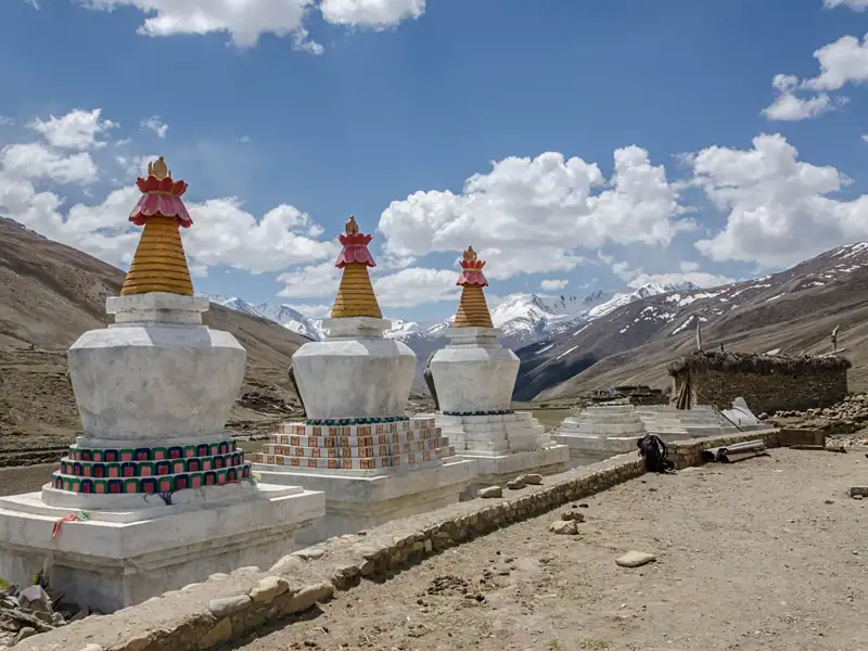 Weiße Stupas mit bunten Verzierungen und schneebedeckte Berge im Hintergrund.