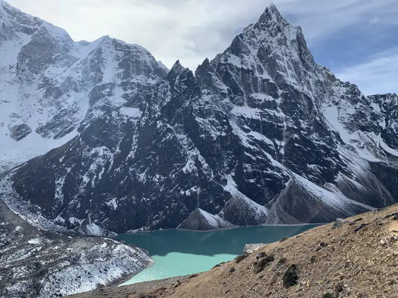 Türkisfarbener Bergsee inmitten schneebedeckter Berglandschaft.