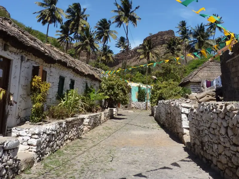 Dorfstraße mit traditionellen Häusern, Palmen und Festtagsdekoration.