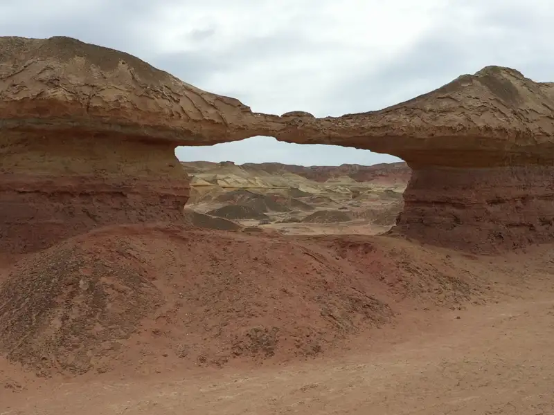 Natürliche Felsbrücke in einer Wüstenlandschaft mit roten und beigefarbenen Gesteinsformationen.