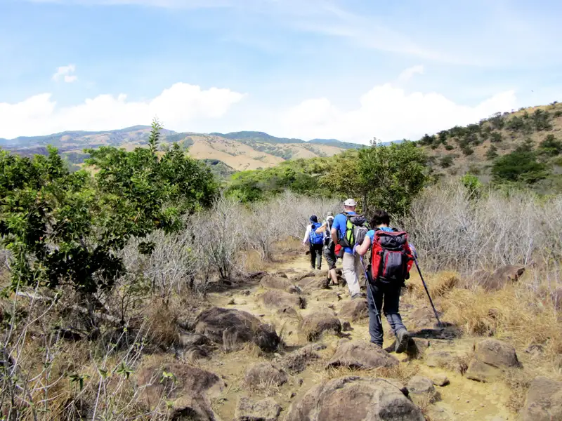 Wanderer auf einem steinigen Weg in hügeliger Landschaft.