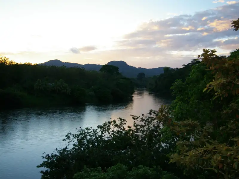 Abendlicher Blick auf den Fluss, umgeben von Bäumen und Hügeln im Hintergrund.